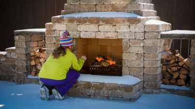 Young girl warmed her hands in front of an outdoor fireplace.
