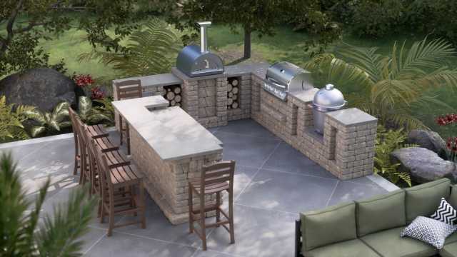 Stone outdoor kitchen with wrap-around bar, wood-fired pizza oven, kamado smoker, and gas grill in an outdoor patio setting