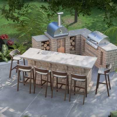 Compact L-shaped outdoor kitchen hardscape kit with wrap-around bar, 32” gas grill, and wood-fired pizza oven, designed for angled corner placement.
